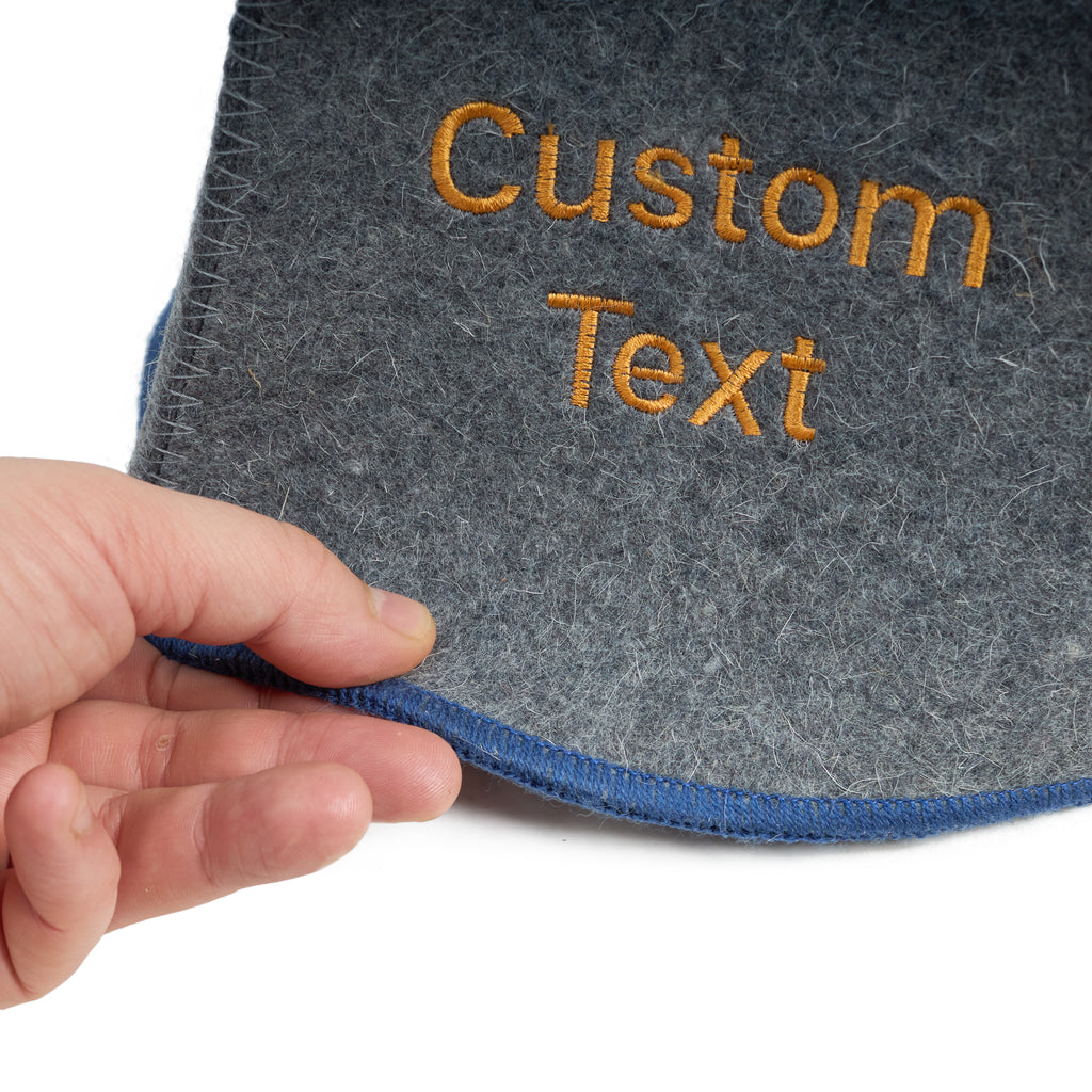 Gray wool sauna hat with blue trim and custom embroidered text, shown close-up in hand