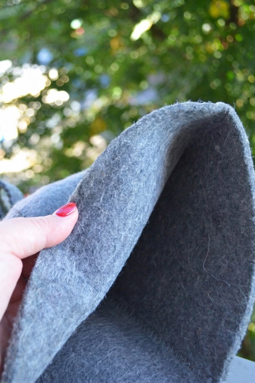 Close-up of gray fabric held by a hand with red nail polish, blurred green foliage in the background
