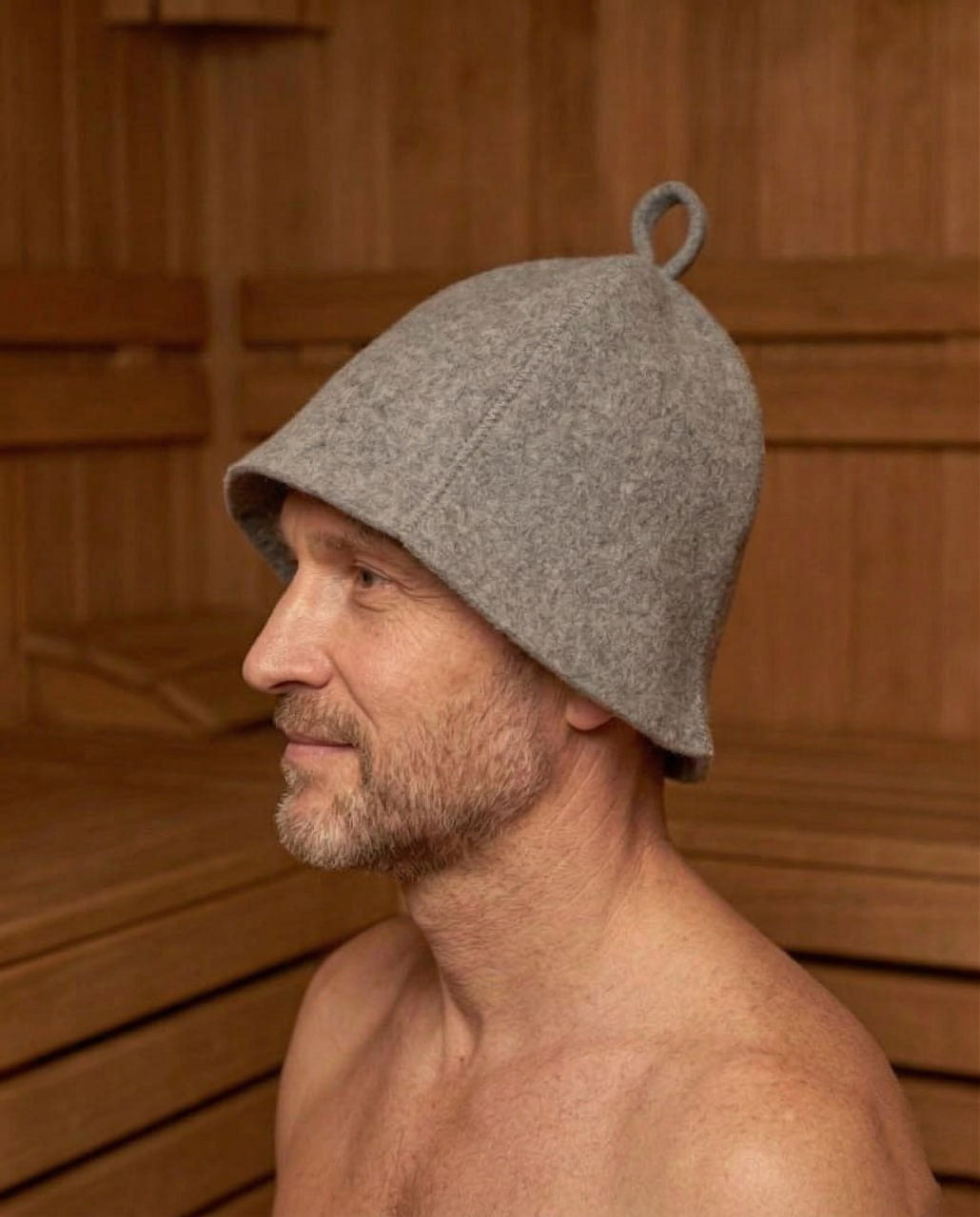 Man wearing a gray sauna hat in a wooden sauna