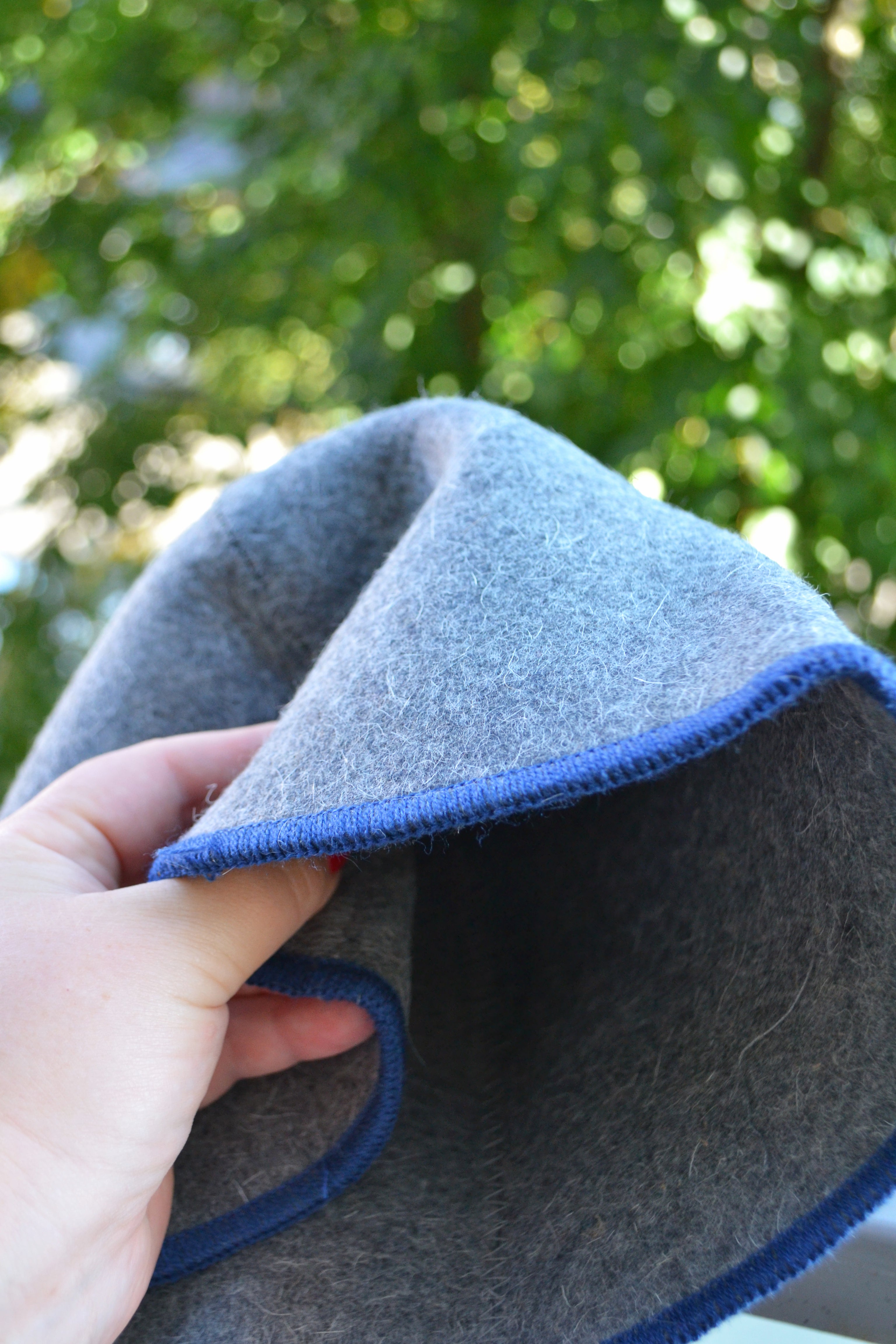 Gray felt with blue edge held by a hand against a blurred green outdoor background