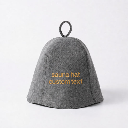 Gray wool sauna hat with orange custom text embroidery on the front, featuring a classic bell shape, visible stitched seams, dense felt texture, and hanging loop at the top