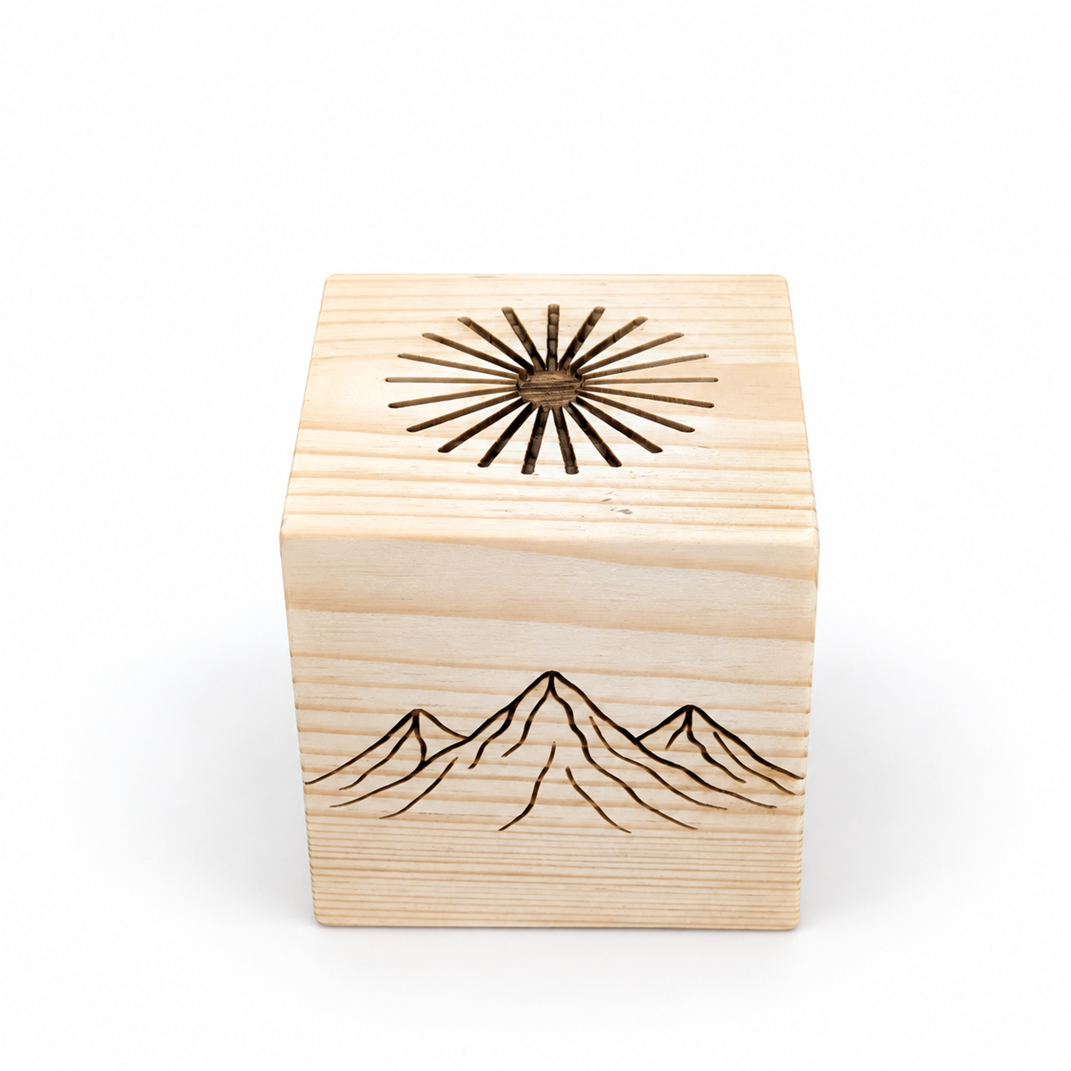 Elevated angled view of a solid pine sauna aromatherapy cube showing the engraved mountain illustration on the front and the complete radial groove pattern on top. The carved channels spread essential oil across the wood as the diffuser warms in the sauna.