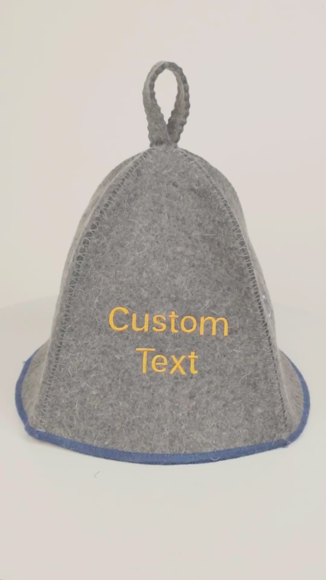 Short product video showing a gray wool sauna hat with blue trim and custom embroidered text on a white background