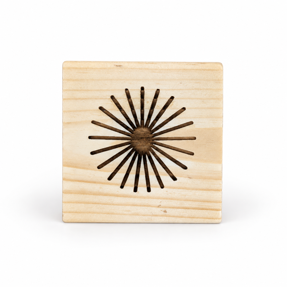 Top view of a square solid pine sauna oil diffuser cube with a small central oil well and dark radial drip grooves extending outward in a sunburst pattern. The carved channels help distribute essential oil over the natural wooden surface for gradual fragrance release