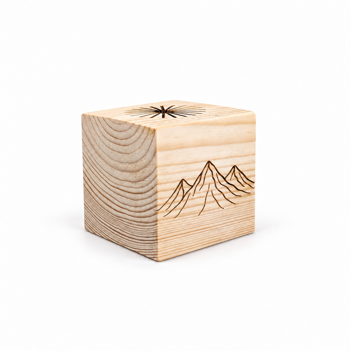Three-quarter view of a solid pine sauna oil diffuser cube on a clean white studio background. The natural wood grain is visible on two sides, with an engraved mountain landscape on the front and radial drip grooves carved into the top for distributing essential oil