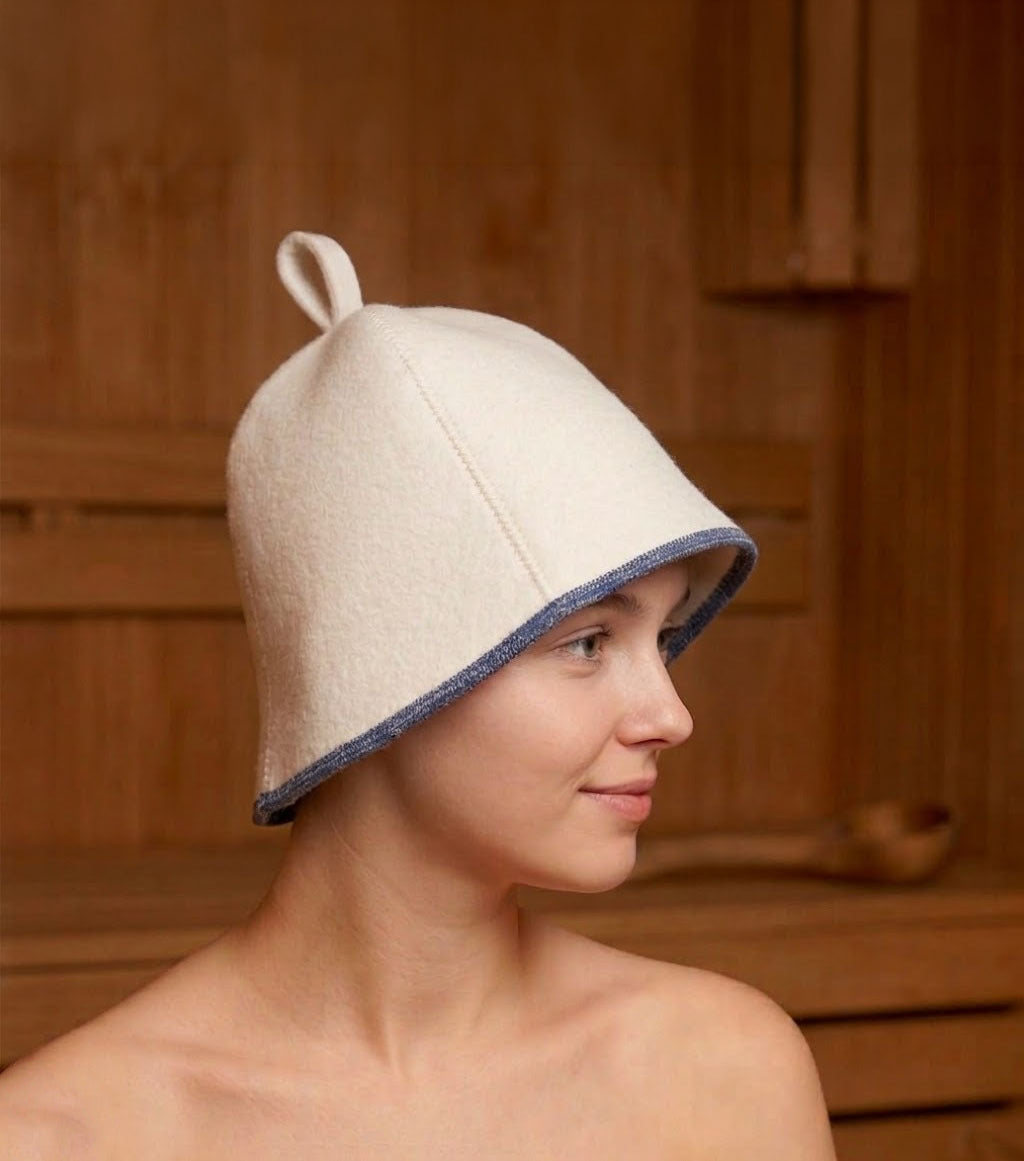 White wool sauna hat with blue trim worn by woman inside a wooden sauna