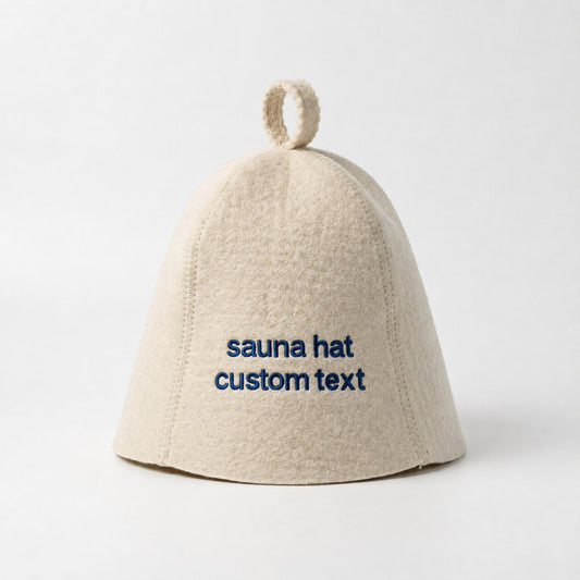 Natural white wool sauna hat with blue custom text embroidery on the front, featuring a classic bell shape, dense felt texture, visible stitched seams, and a hanging loop at the top