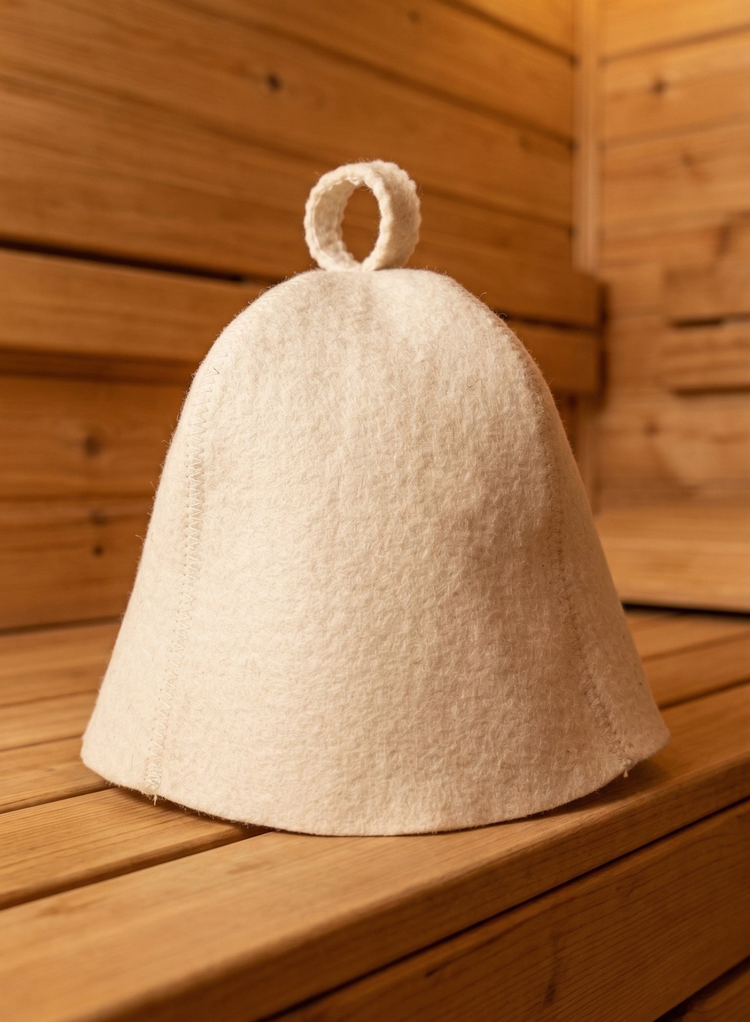White wool sauna hat on wooden bench inside sauna with natural wood interior
