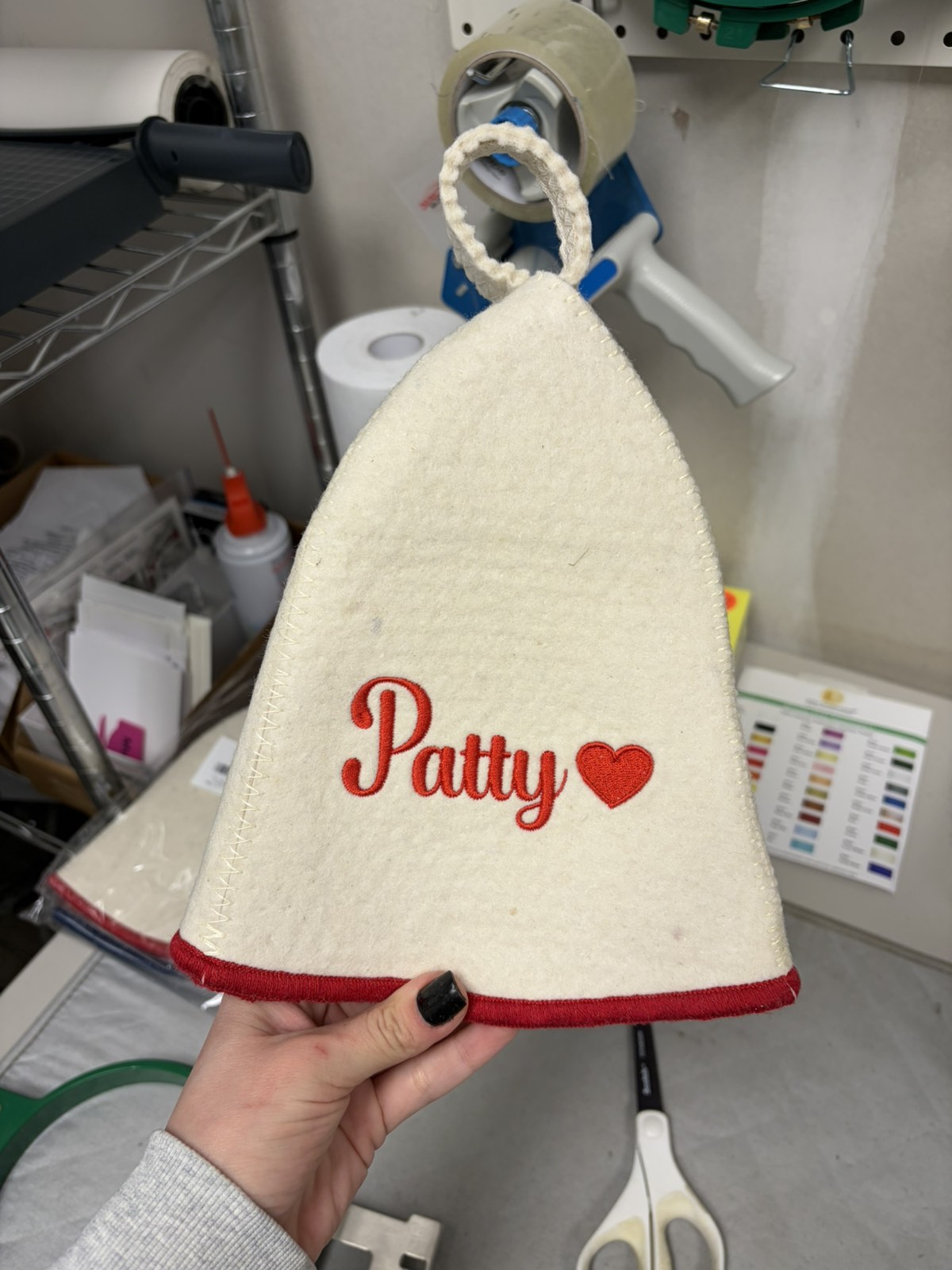 White wool sauna hat with red trim and red Patty name embroidery with a heart, held by hand in a workshop setting