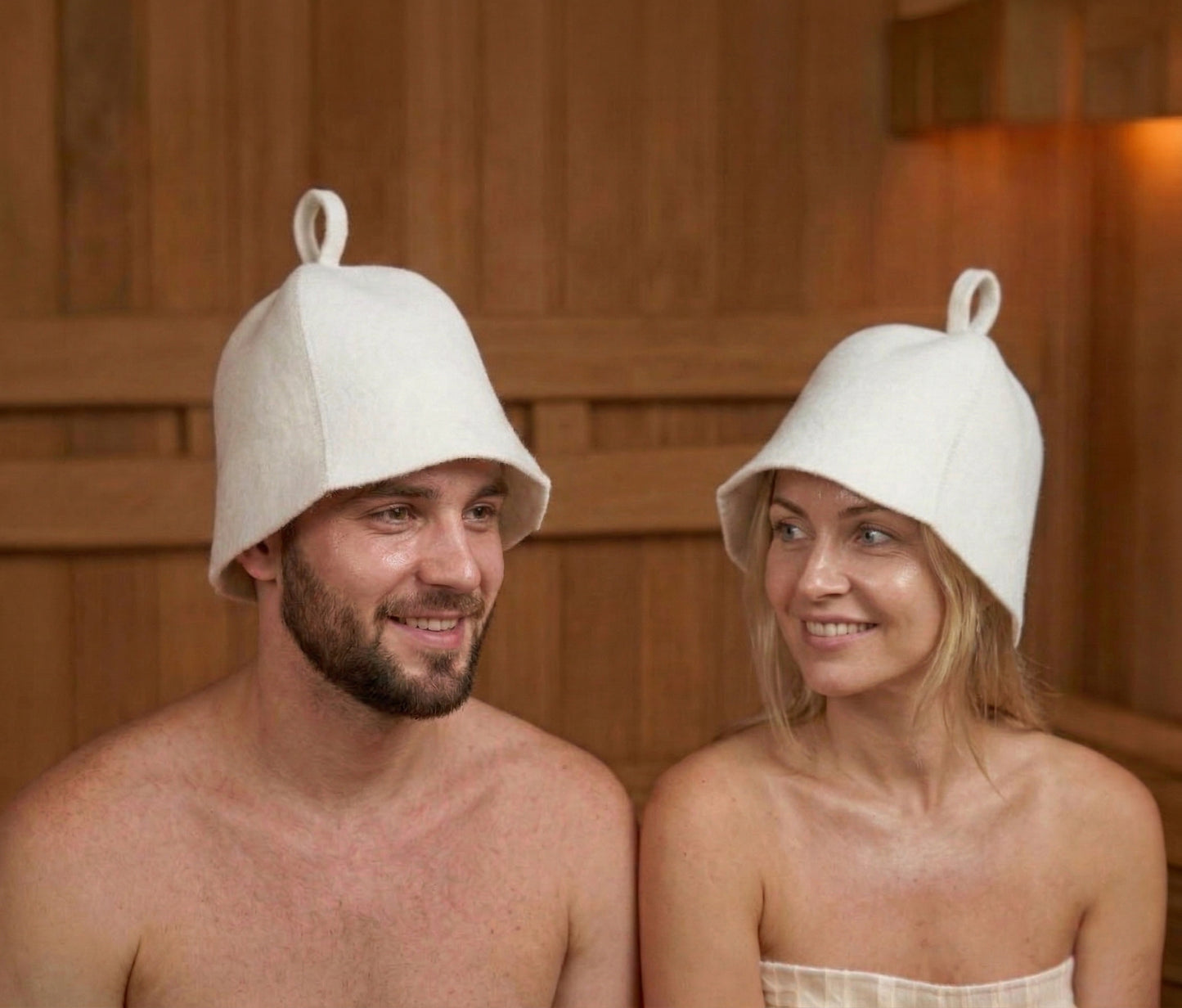 Man and woman wearing white wool sauna hats sitting inside a wooden sauna
