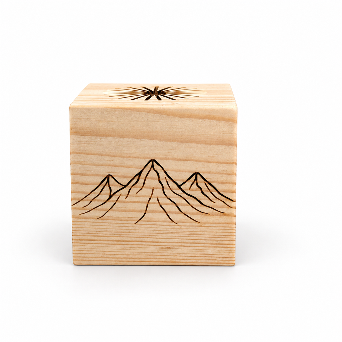 Front view of a square wooden sauna essential oil diffuser made from light solid pine. The cube features a dark engraved mountain motif across the front, natural horizontal wood grain, and a partially visible sunburst-shaped oil channel design on top